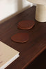 Set aus braunen, asymmetrischen Lederuntersetzern in modernem Wohnzimmer-Ambiente, mit Tasse Cappuccino auf einem Untersetzer